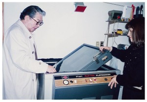 暗室にて。細江館長（左）が動かしているのは、ヴァキュームによってネガと印画紙を密着させ、ガラス版を回転させて露光するプリント用機器。
